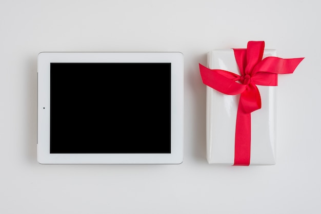 Tablet near gift box with red ribbon