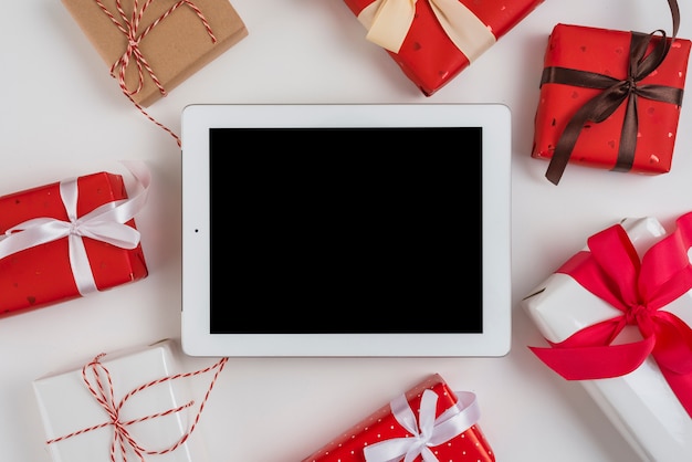 Tablet near set of gift boxes with ribbons and twists 