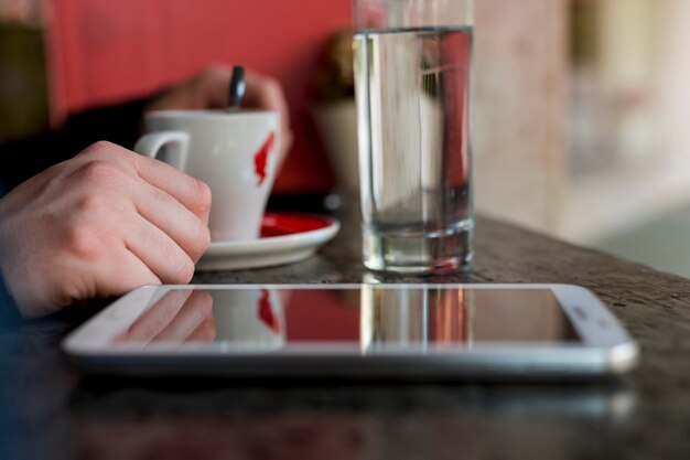 Tablet placed on table near cup with beverage