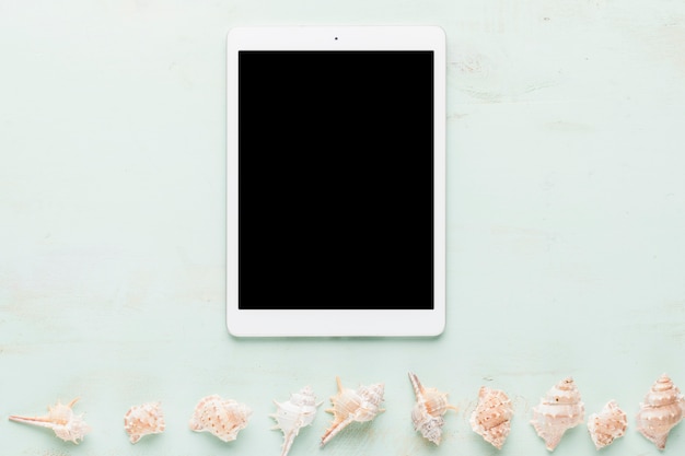 Tablet and row of seashells on light background