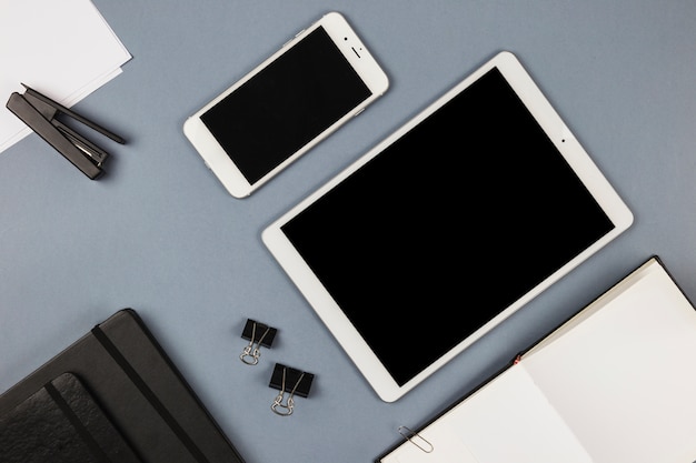 Tablet and smartphone with notebook on grey table