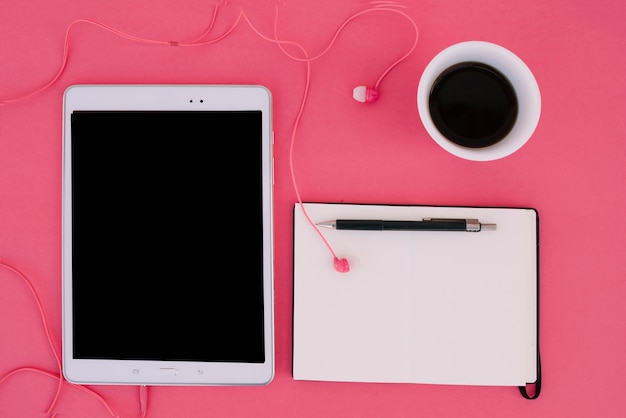 Tablet with earphones near notebook and coffee