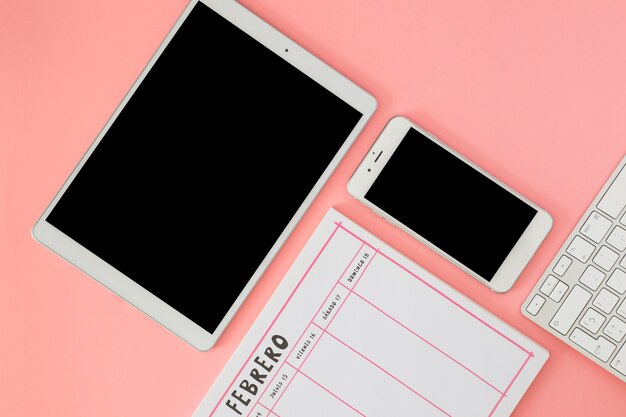 Tablet with smartphone and notebook on pink table