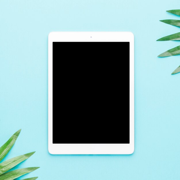 Tablet with tropical leaves on light background