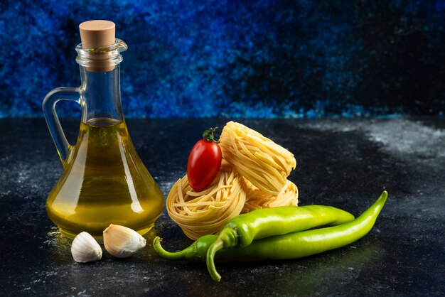 Tagliatelle nests, oil and vegetables on marble surface.