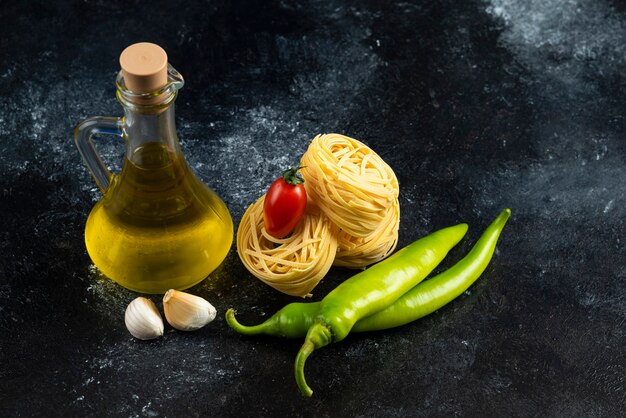 Tagliatelle nests, oil and vegetables on marble surface.