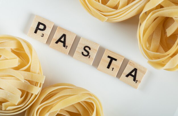 Tagliatelle nests on white surface with wooden letters.