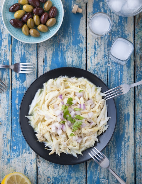 Tagliatelle pasta in a black plate near a plate of olives on a wooden table