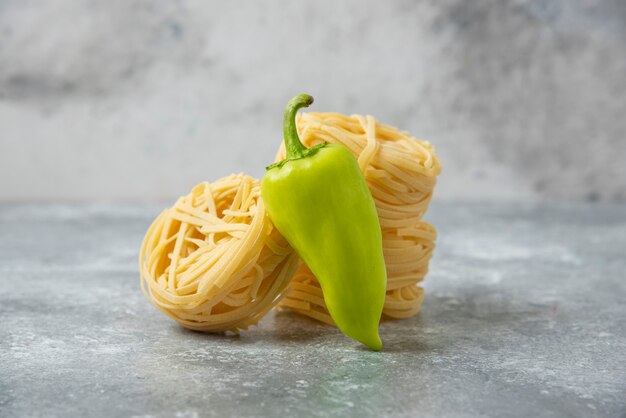 Гнезда из сырых макарон Tagliatelle и зеленый перец на мраморном столе.