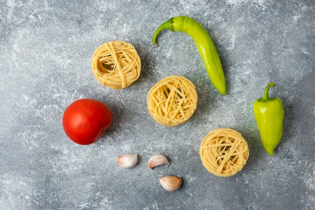 Tagliatelle raw pasta nests and vegetables on marble table. 