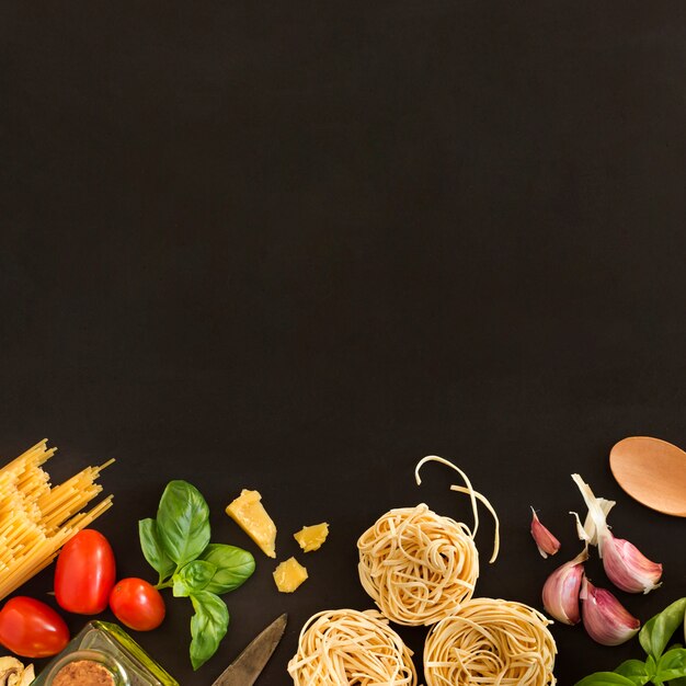 Tagliatelle and spaghetti pasta with ingredients on black background