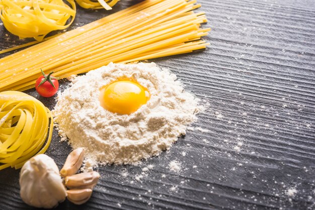 Tagliatelle and spaghetti pasta with ingredients on wooden plank backdrop