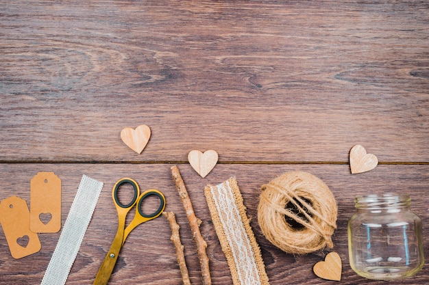 Tags; ruler; scissor; sticks; lace ribbon; empty jar and heart shape on wooden backdrop