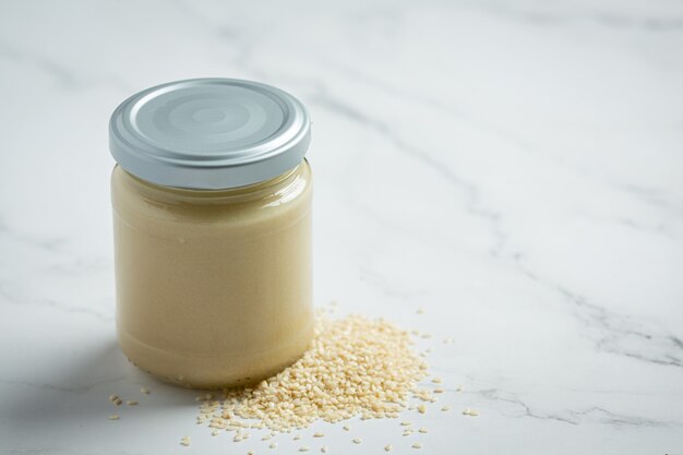 Tahini and sesame seeds on marble background