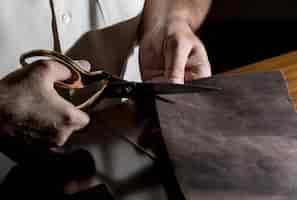 Free photo tailor cutting leather with scissors