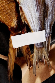 Tails on smoked and airdried salted fish with label on black backdrop with kraft paper