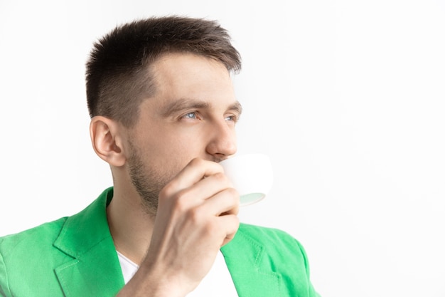 Taking a coffee break. Handsome young man holding coffee cup, smiling while standing against gray walll