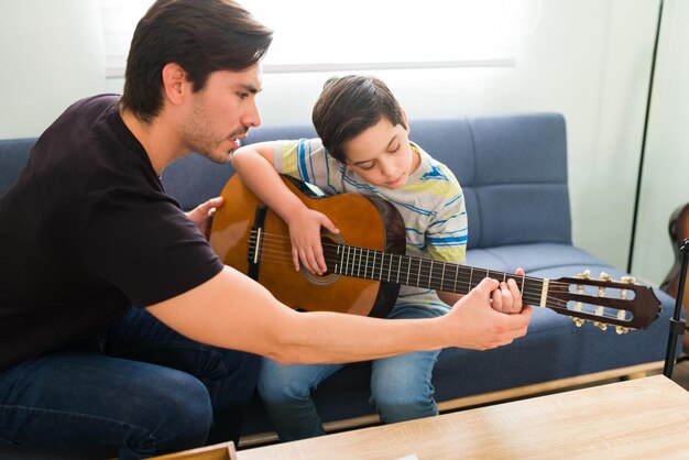 개인 음악 선생님과 함께 기타 수업을 듣습니다. 히스패닉 청년은 가정 수업 중에 초등학교 소년이 기타를 칠 수 있도록 도와줍니다.