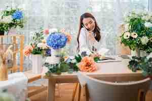 Free photo taking order florist working from homeyoung asian florist making list from client order to arrange flower bouqet vase delivery flower design store happiness smiling young lady making flower vase