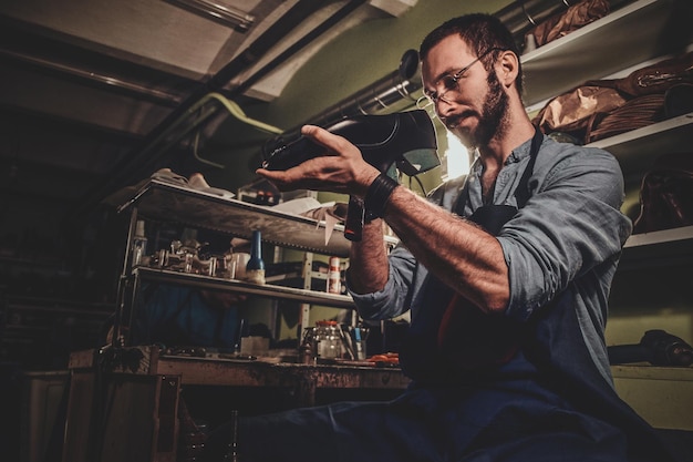 Talented cobbler is working on pair of black men's shoes at his workshop.