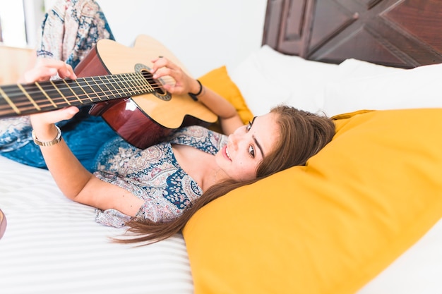 Талантливая девушка, лежащая на кровати, играющая на гитаре