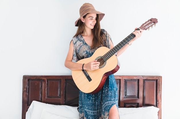 Бесплатное фото Талантливая девушка, стоящая на кровати, играющая на гитаре