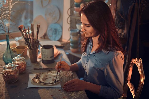 Талантливая молодая женщина работает над новой декоративной тарелкой в своей уютной мастерской.