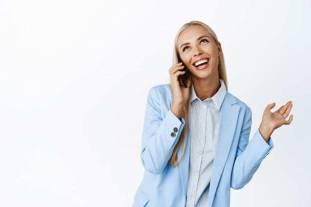 수다스러운 귀여운 여성 사업가가 휴대폰으로 웃고 흰색 배경 위에 서서 행복한 대화를 나누는 모습