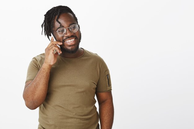 Talkative guy with glasses posing against the white wall with his phone