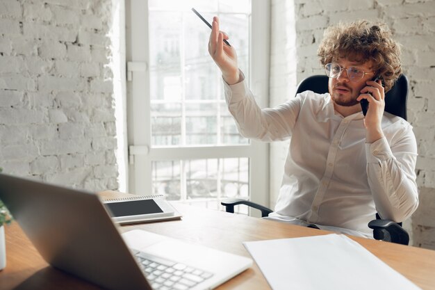 Talking on phone. Caucasian young man in business attire working in office