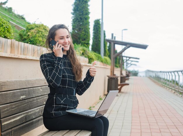 スマートフォンのブロガーの女の子と話すことは公園で完璧なジェスチャーを示しています