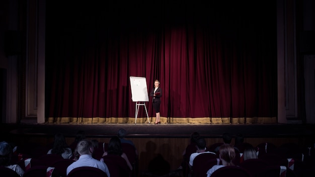 Talking to students. Female speaker giving presentation in hall at workshop. Business centre. Rear view of participants in audience. Conference event, training.