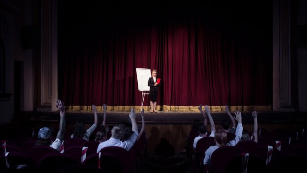 Talking to students. Female speaker giving presentation in hall at workshop. Business centre. Rear view of participants in audience. Conference event, training.