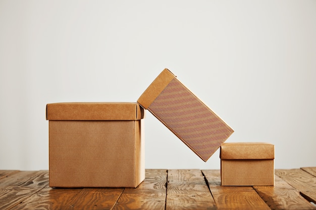 A tall cardboard box balanced on top of two similar boxes with covers in a studio setting isolated on white