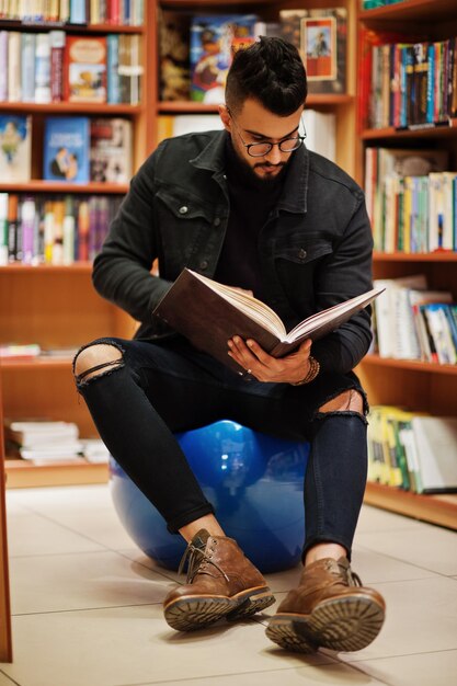 Tall smart arab student man wear on black jeans jacket and eyeglasses sitting at library and read book at hands