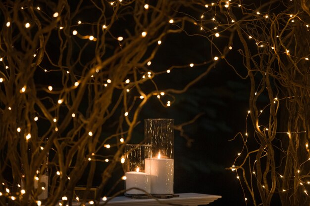 Tall vases with white candles stand under shiny branches