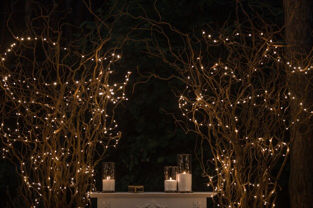 Tall vases with white candles stand under shiny branches