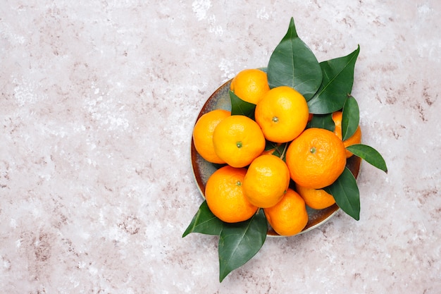 Tangerines (oranges, clementines, citrus fruits) with green leaves on concrete surface with copy space