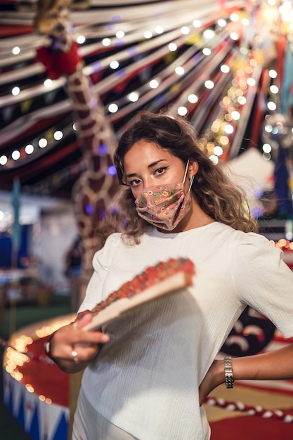 Tanned Caucasian female wearing a floral mask and holding a fan at an amusement park