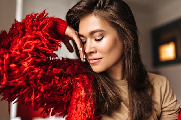 Tanned dark-haired woman in beige T-shirt leaned against wall. Portrait of attractive lady wearing red jacket.