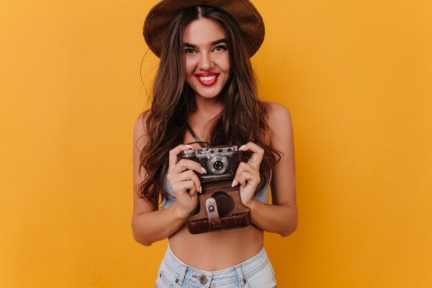 Tanned female photographer with beautiful smile standing on yellow space