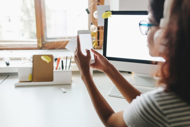 その上にコンピューターとテーブルに座っているスマートフォンを使用してストライプの夏のシャツの日焼けした女の子