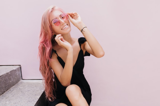 tanned girl touching her sunglasses while posing on the steps.