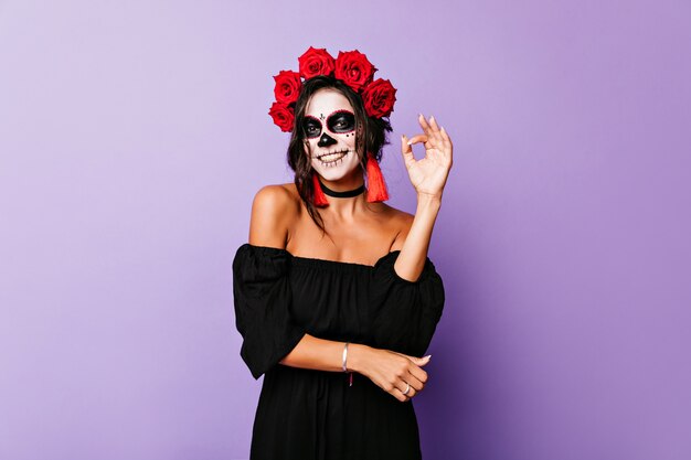 紫の壁に身も凍るような黒い髪の日焼けした笑顔の女の子。写真撮影を楽しんでいる仮面舞踏会の衣装を着た陽気な若い女性。