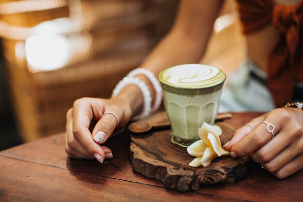 Tanned woman sits in cafe and poses cup of matcha green tea with milk