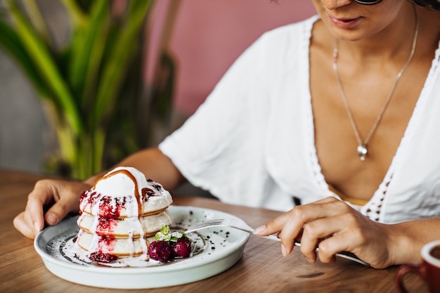 Загорелая женщина в белой футболке держит вилку и ест вкусный десерт