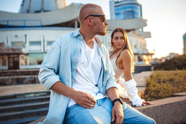 Tanned young caucasian couple, modern lovestory in film grain effect and vintage style. Sunset time. Walking on the city's street, summer warm evening. Honeymoon concept. Toned in teal orange.