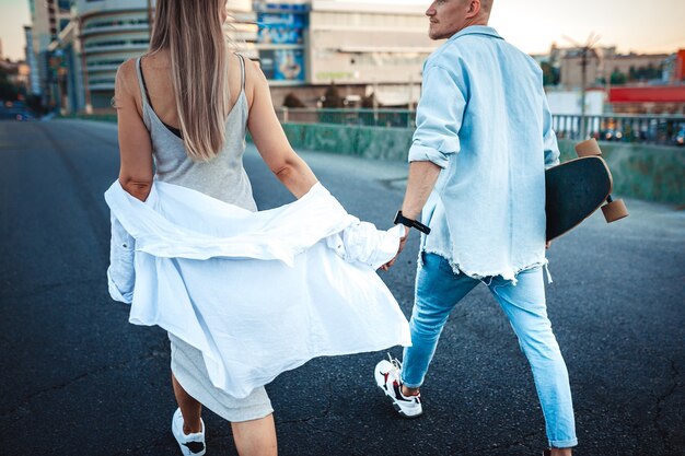 Tanned young caucasian couple, modern lovestory in film grain effect and vintage style. Sunset time. Walking on the city's street, summer warm evening