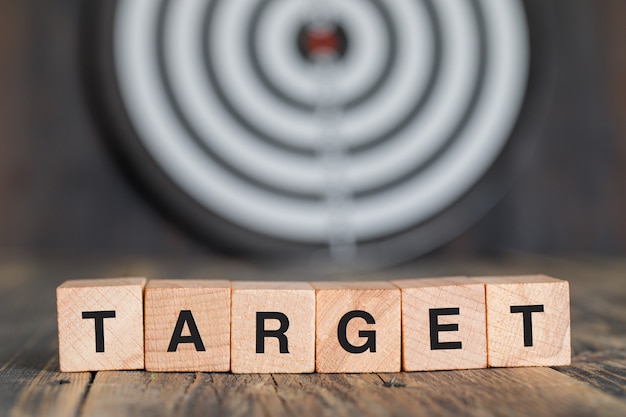 Targeting concept with dartboard, wooden cubes on wooden table side view.