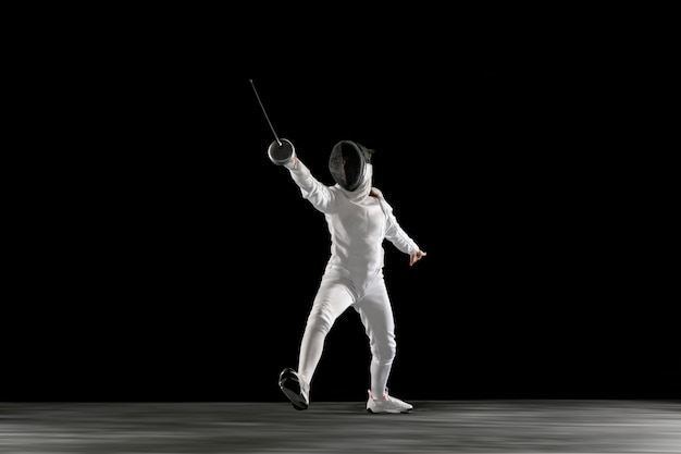 Targets. Teen girl in fencing costume with sword in hand isolated on black